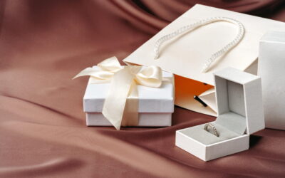 Un coffret cadeau bijou ouvert contenant une bague solitaire en argent sur un lit de satin marron.