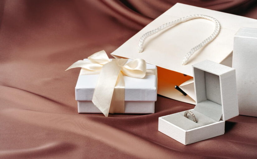 Un coffret cadeau bijou ouvert contenant une bague solitaire en argent sur un lit de satin marron.