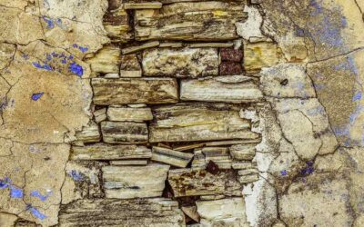 Surface craquelée avec des pierres et du plâtre partiellement effrités, taches bleues éparpillées