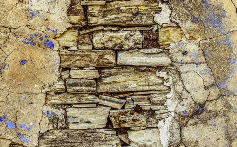 Surface craquelée avec des pierres et du plâtre partiellement effrités, taches bleues éparpillées