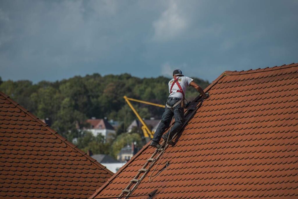 Couvreur équipé de sécurité travaillant sur une toiture en tuiles rouges avec vallée