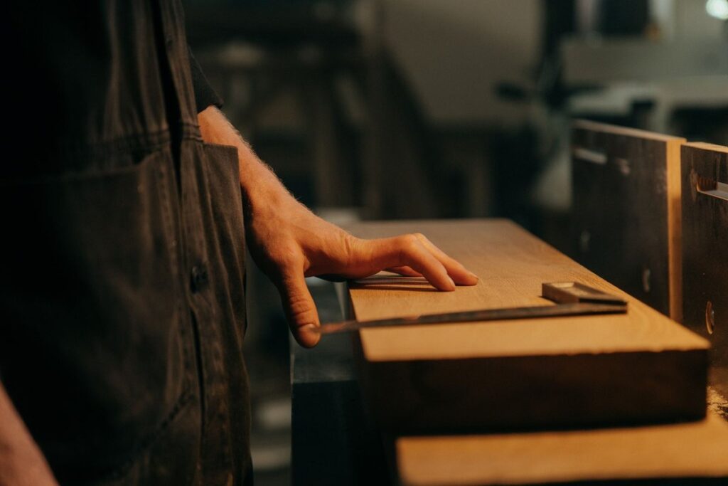 Main posée sur une planche en bois avec un outil, dans un atelier