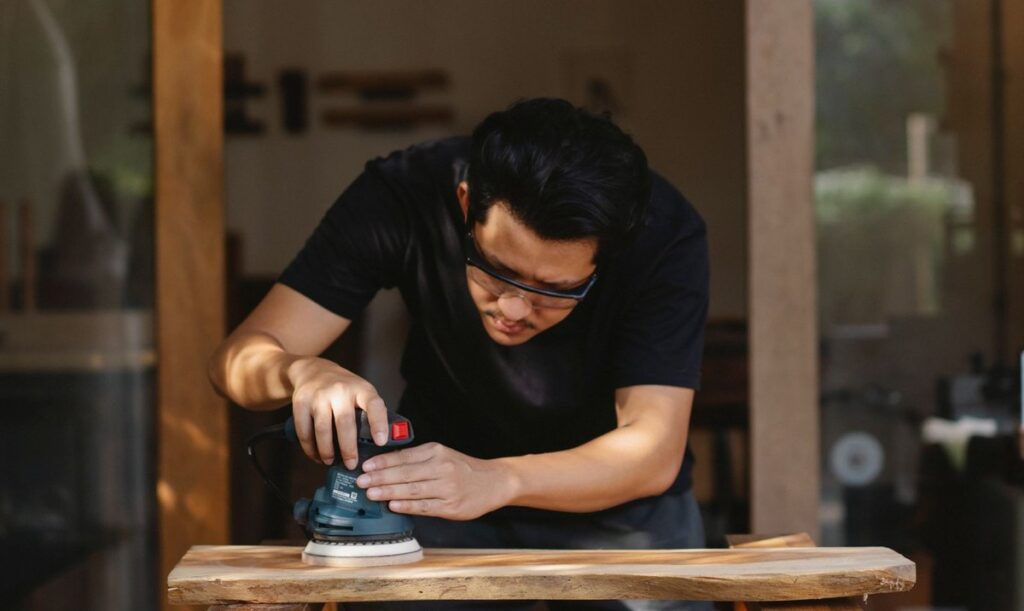 Homme ponçant une table en bois dans un atelier, lunettes de protection