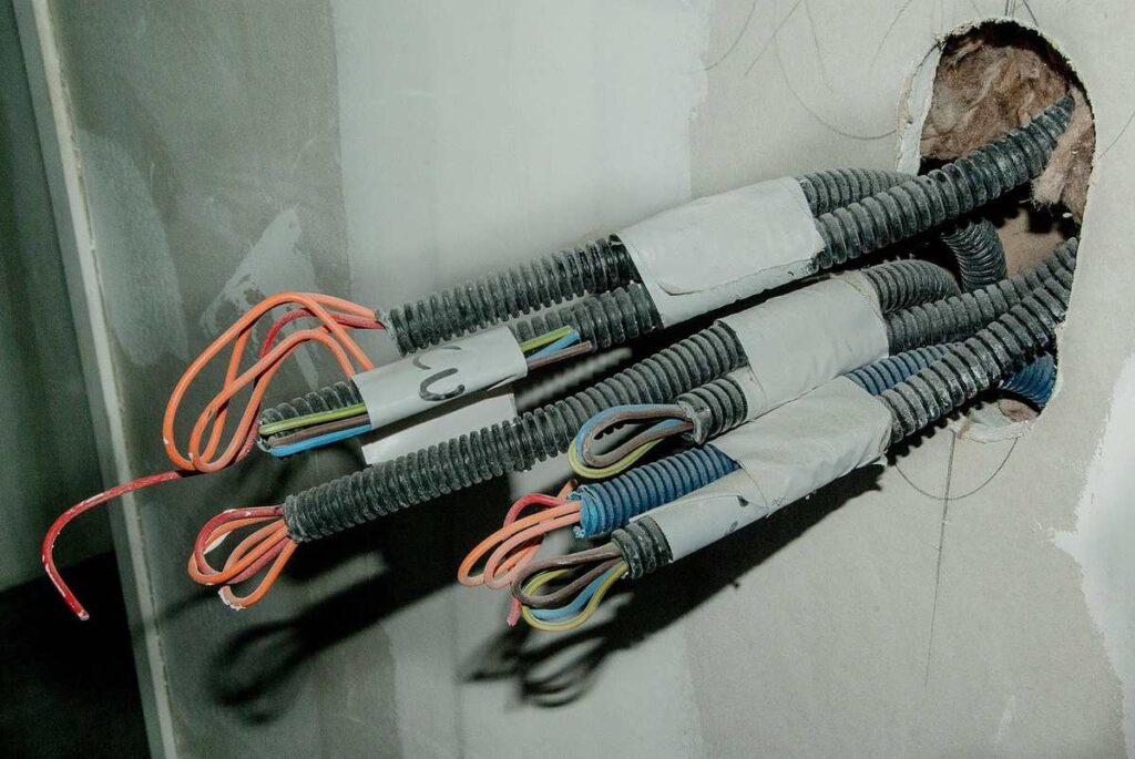 Câbles électriques sortant d'un trou dans un mur, avec des fils orange et bleu