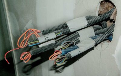Câbles électriques sortant d'un trou dans un mur, avec des fils orange et bleu