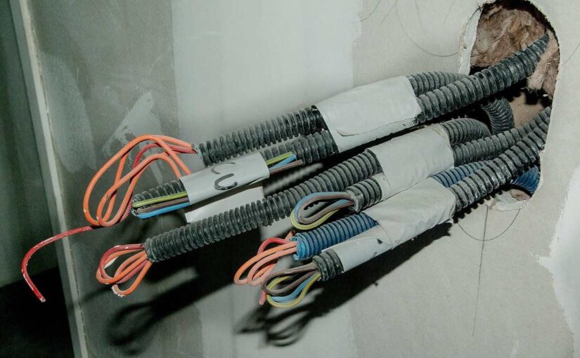 Câbles électriques sortant d'un trou dans un mur, avec des fils orange et bleu