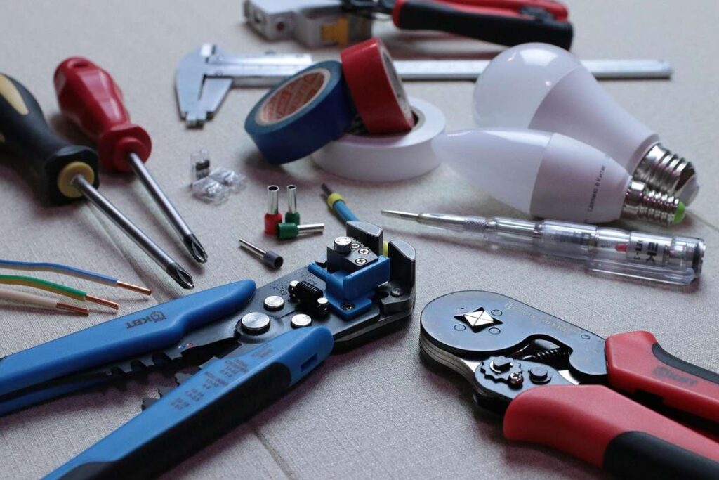 Outils de bricolage sur une table, y compris des pinces, des ciseaux, des ampoules et des fils électriques