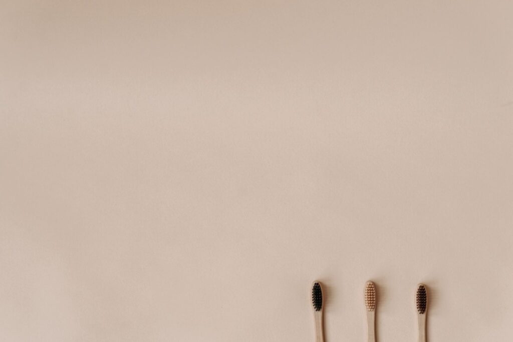 Trois brosses à dents à manches naturels beige avec têtes noires alignées sur fond neutre