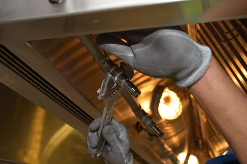 Mains gantées ajustant des tuyaux sous un appareil métallique dans un environnement industriel