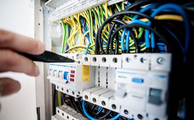 Une main utilise un tournevis pour vérifier le tableau électrique