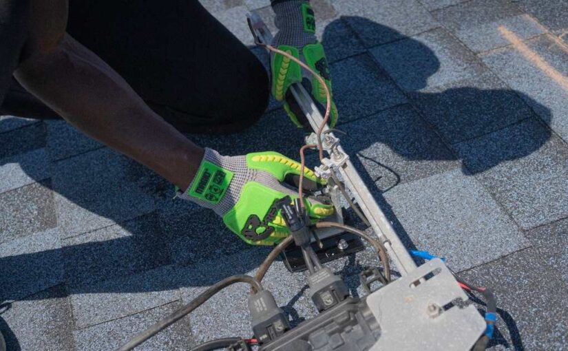 Technicien en gants jaunes ajuste un équipement avec câbles sur un revêtement gris
