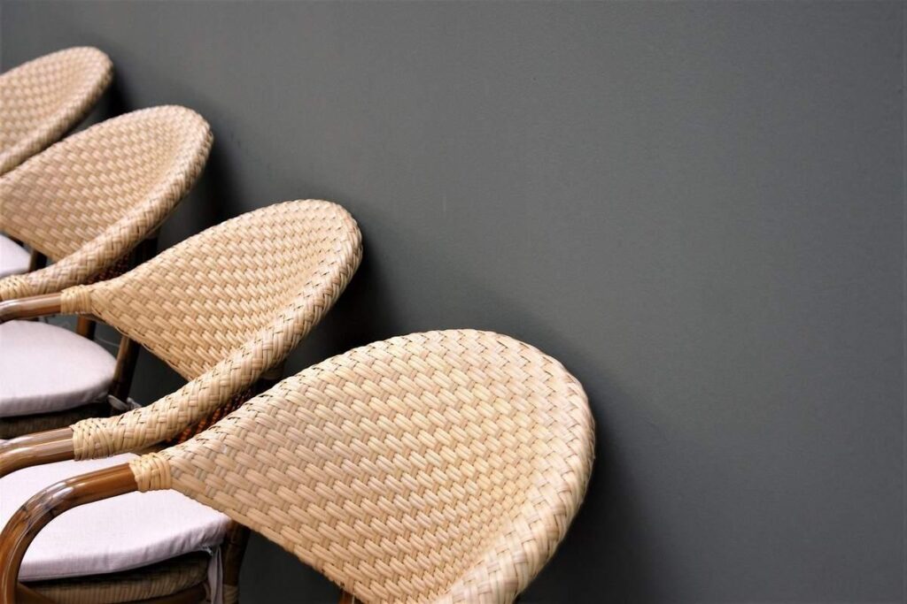 Quatre chaises en rotin avec coussins blancs contre un mur sombre